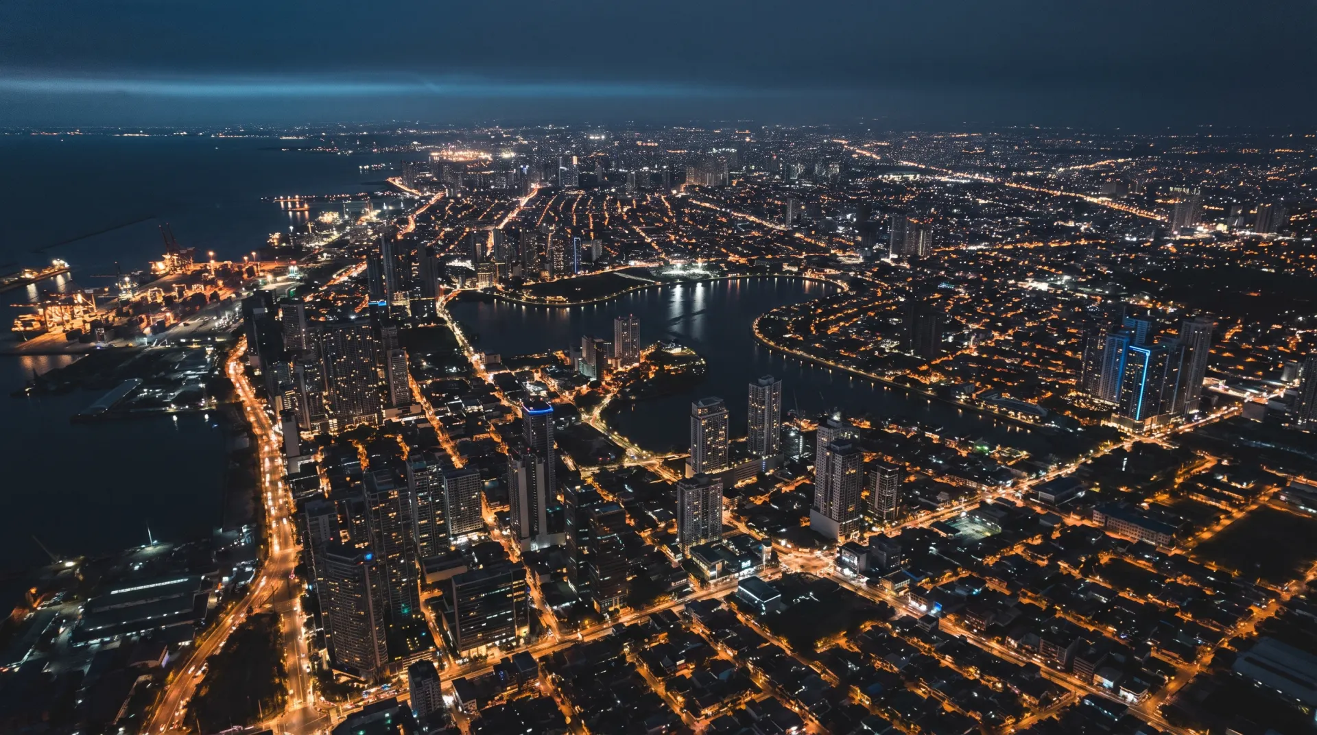 Manila at night from two kilometers up, amber street grid meeting the bay